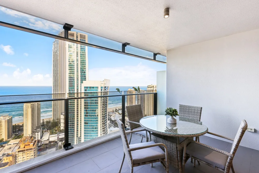 A balcony dining area overlooks the ocean and nearby high-rise buildings.