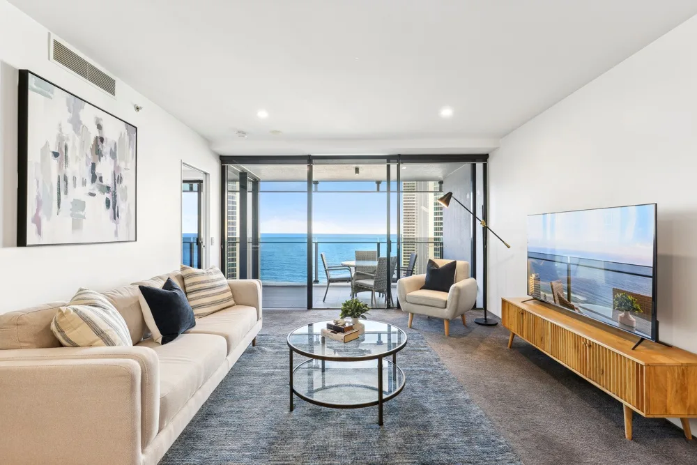 A living room with seating, a television, and ocean views through glass doors.