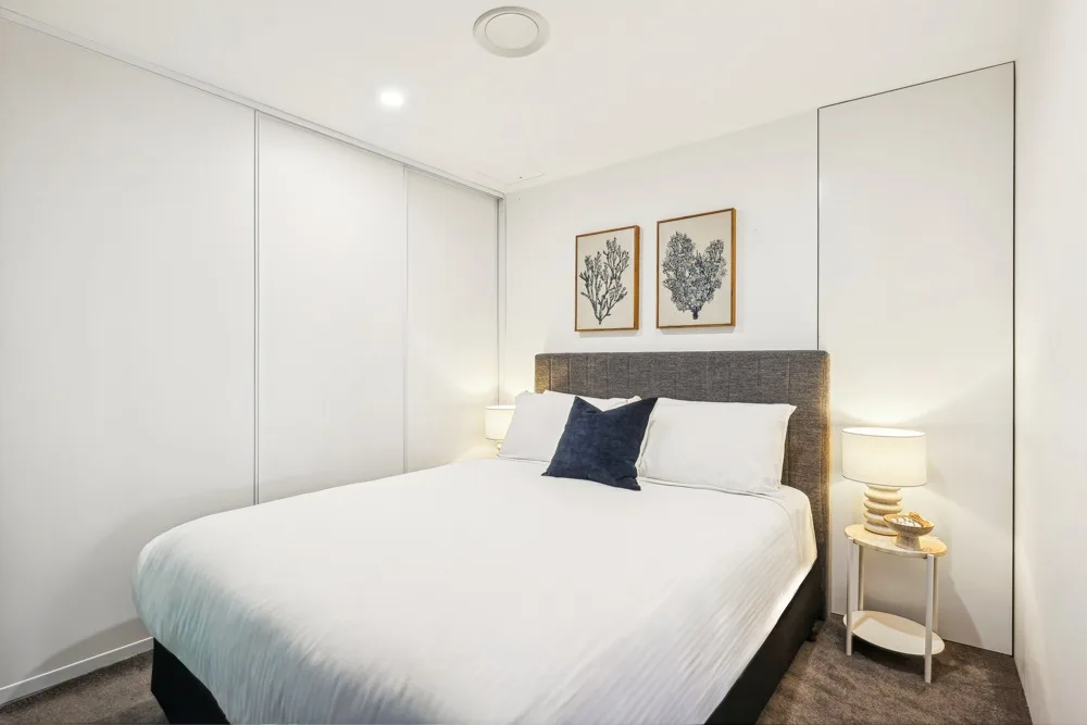 A bright bedroom with a neatly made bed and framed artwork above the headboard.
