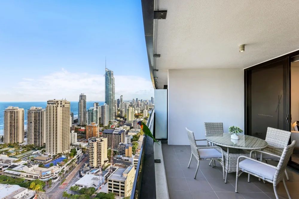 A balcony seating area overlooks a dense city skyline and the ocean.
