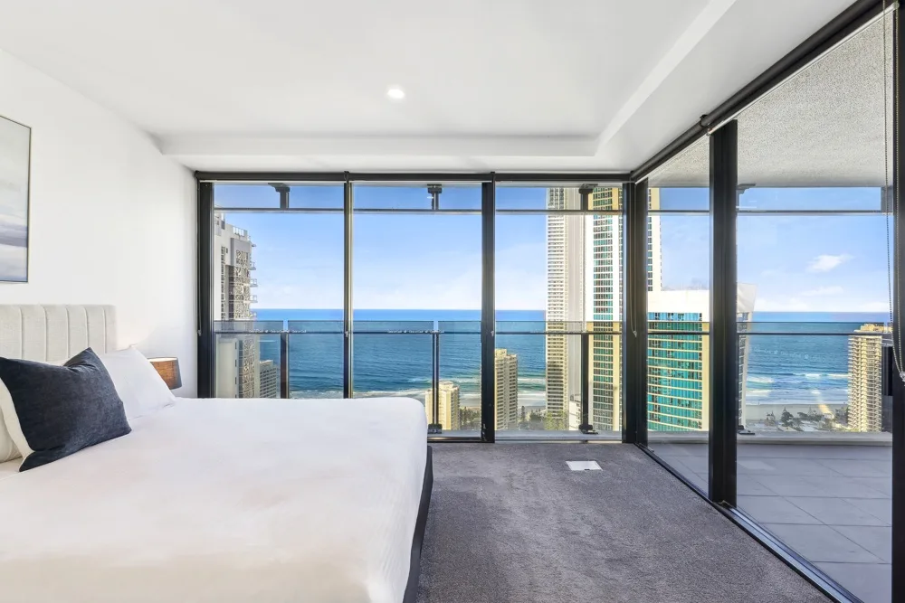 A bedroom with a bed beside floor-to-ceiling windows overlooking the ocean.