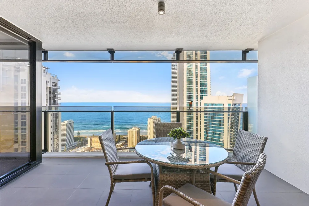 A balcony dining area overlooks the ocean and nearby high-rise buildings.