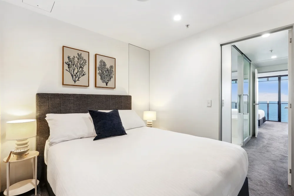 A bright bedroom with a neatly made bed and framed botanical prints above the headboard.