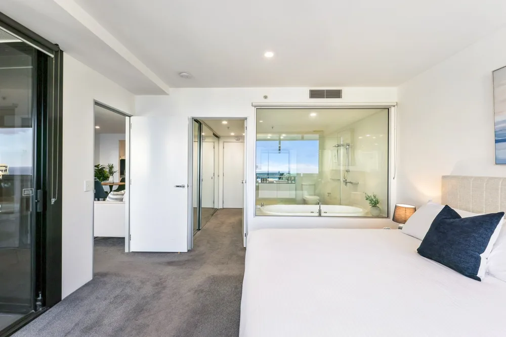A bright bedroom with a bed beside a glass-walled bathroom.
