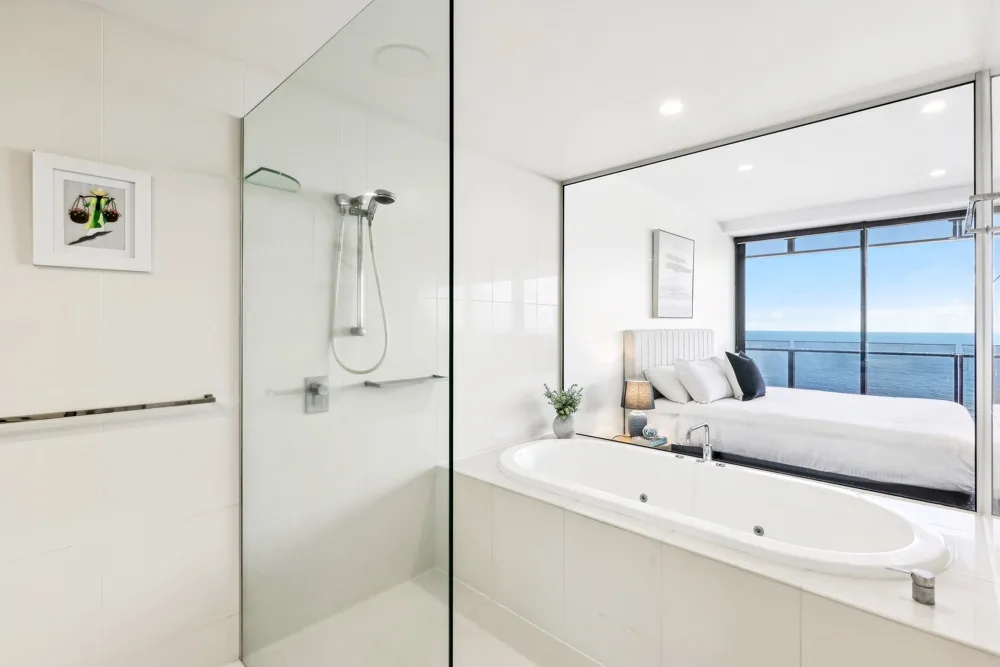 A bright bathroom with a bathtub beside a glass shower and a large window.