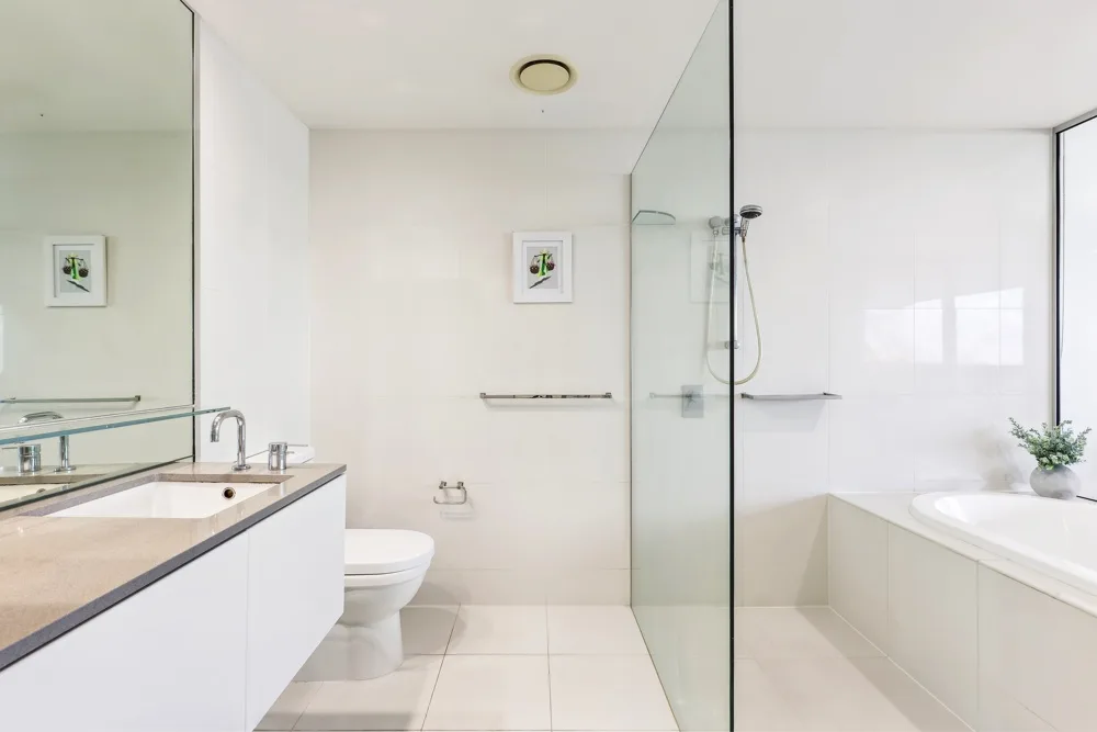 A bright bathroom with a vanity, toilet, and glass shower.