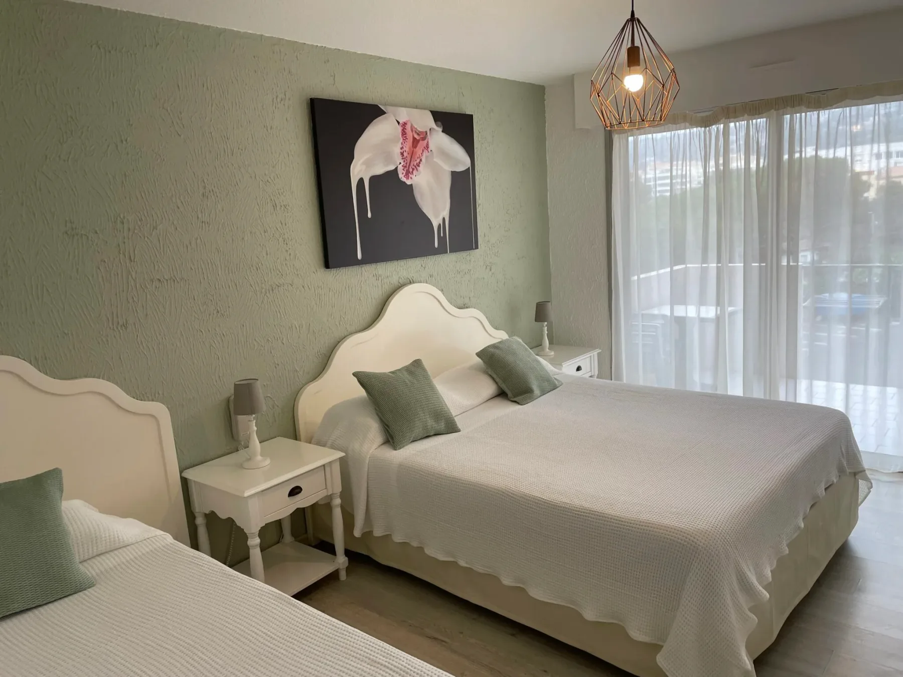 Espacio representativo del hotel: Un dormitorio con dos camas, cojines verdes y cortinas translúcidas.