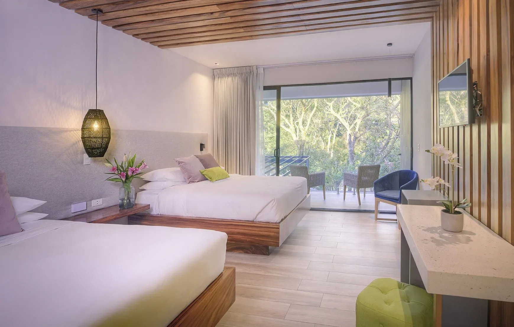 Espacio representativo del hotel: Dormitorio con dos camas y un escritorio junto a una puerta de vidrio con vegetación al fondo.