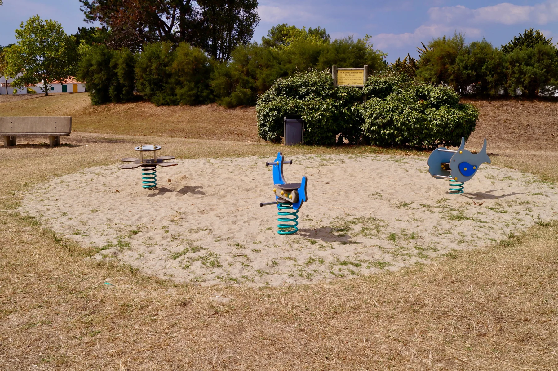 Shared amenity: A playground with spring riders and a bench on dry grass.