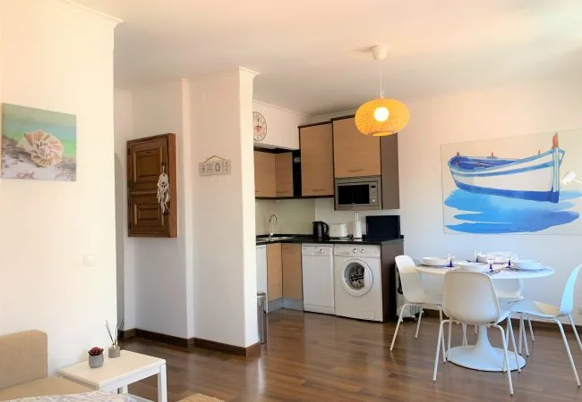 A bright open-plan kitchen and dining area with a round table and blue boat artwork.
