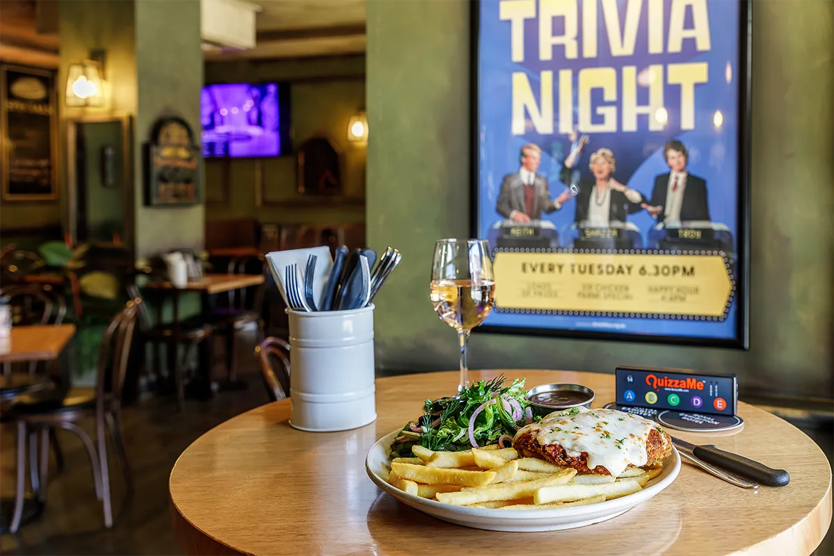 Representative hotel space: A restaurant table holds a plated meal beside a Trivia Night poster.