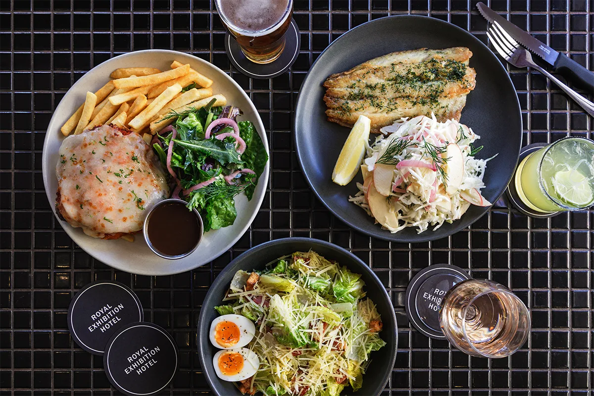 Representative hotel space: A meal spread with plated food, salad, drinks, and cutlery on a dark table.