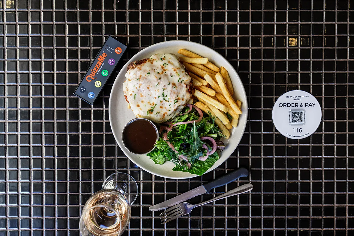 Representative hotel space: A plated meal with fries, greens, and a small sauce cup on a dark grid table.