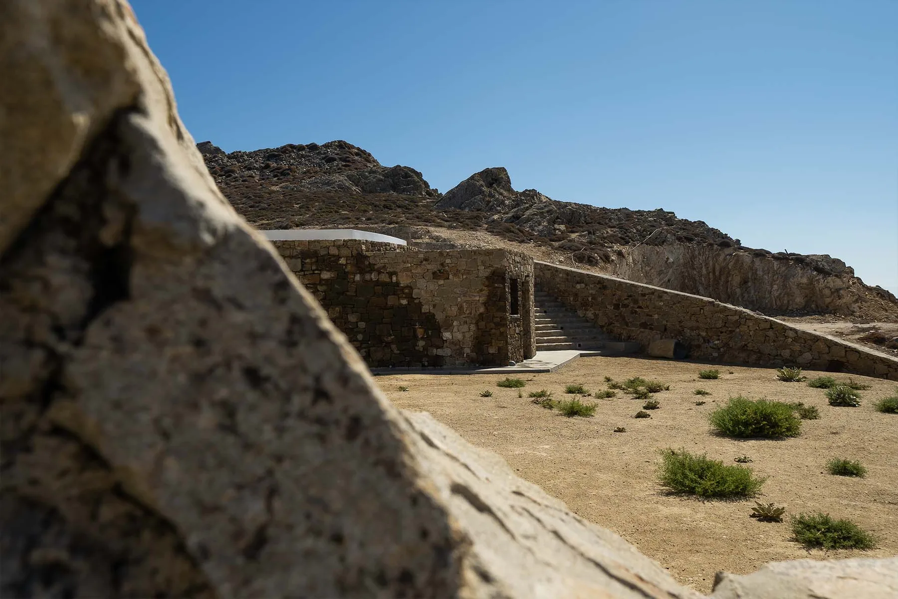 A stone stairway rises beside a low stone wall in a dry, rocky landscape.