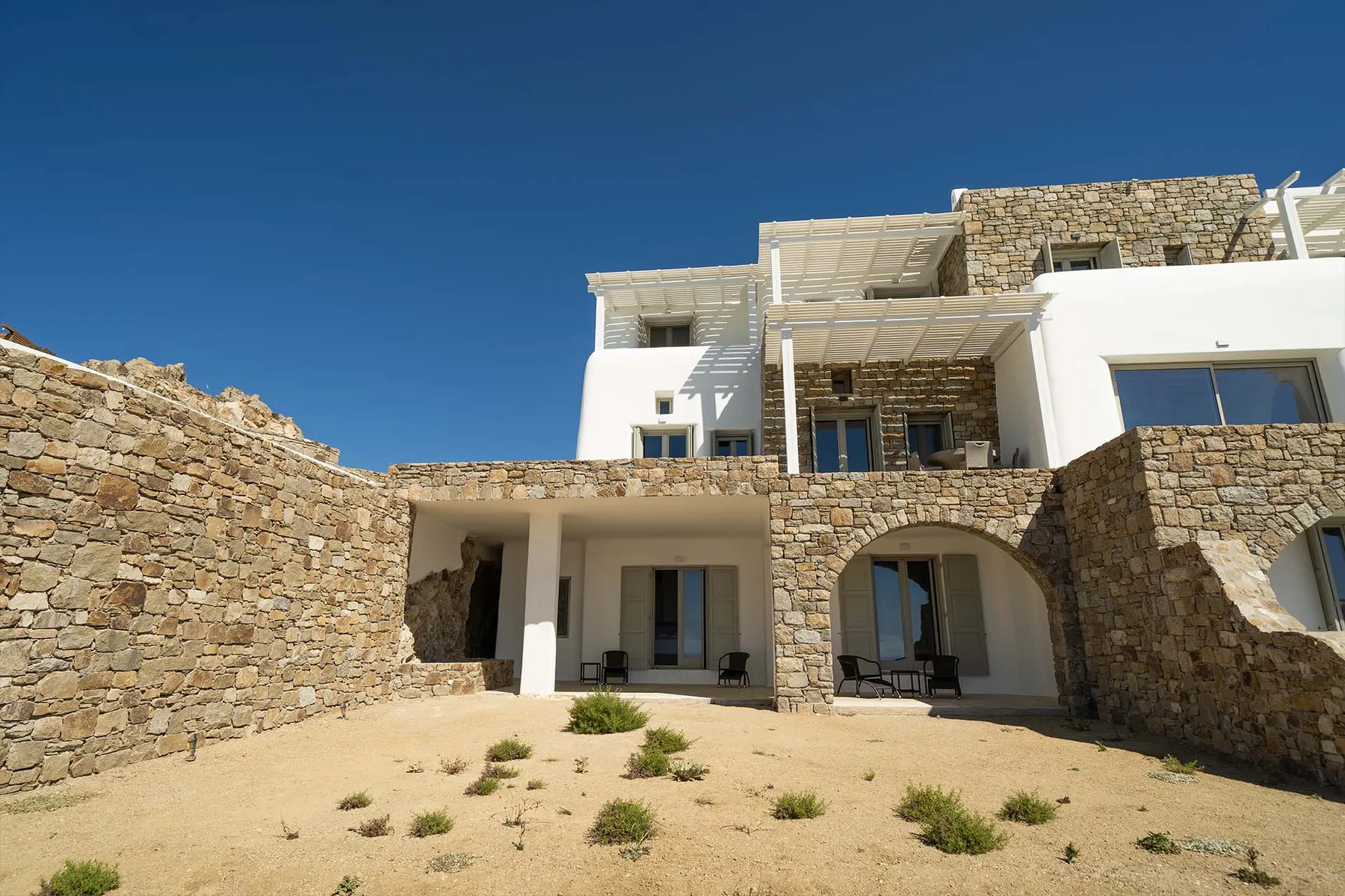 A white and stone building opens onto a sandy courtyard with sparse plants.