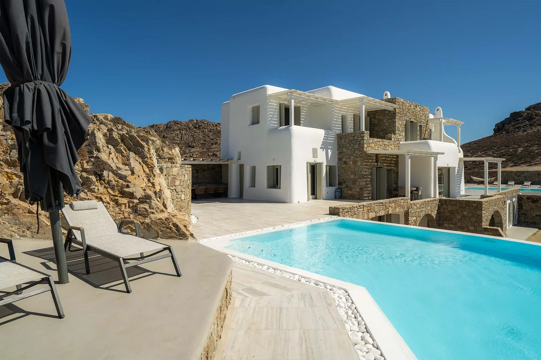 A modern house overlooks a swimming pool, with lounge seating on the patio.