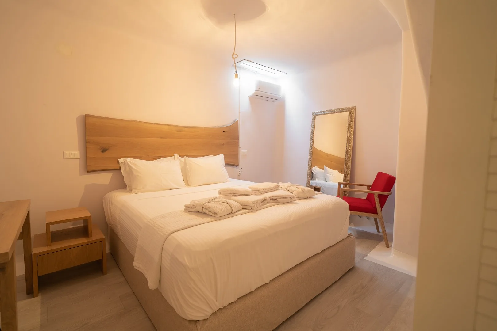 A bedroom with a neatly made bed and a red chair beside a mirror.