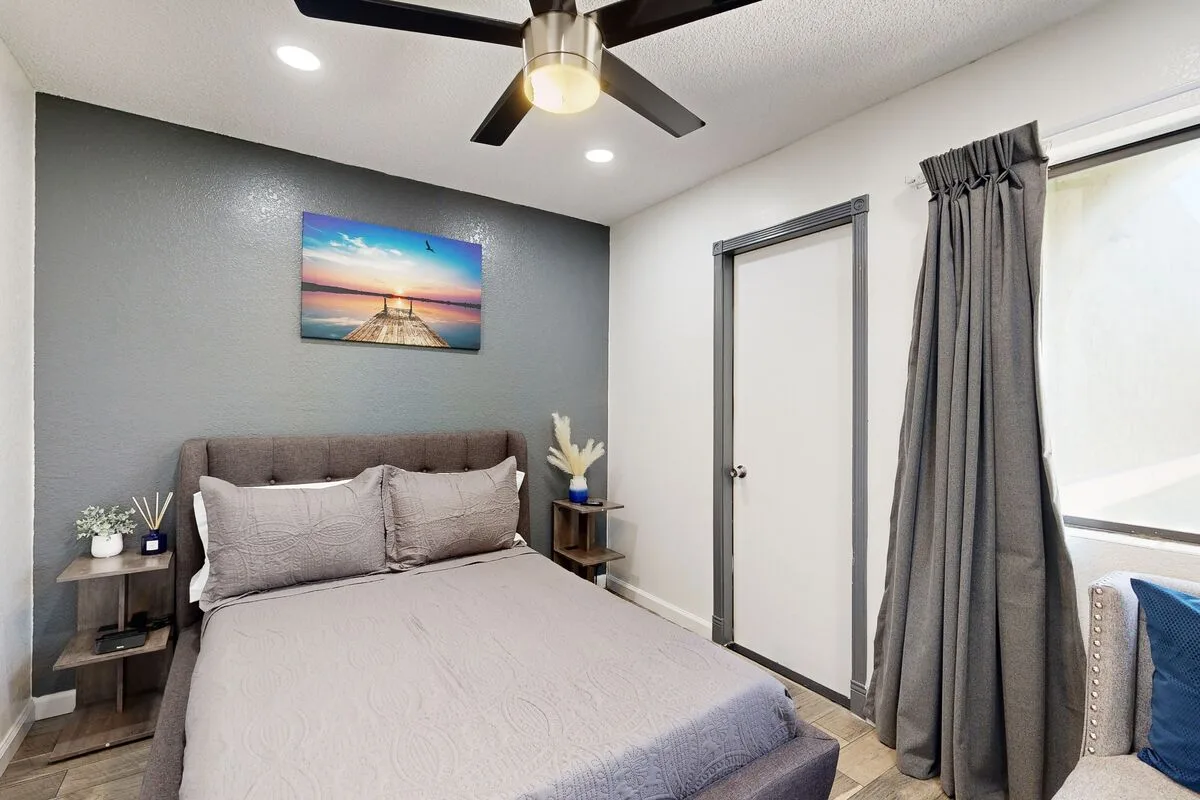 Un dormitorio con una cama junto a una pared de acento gris y una ventana con cortinas.