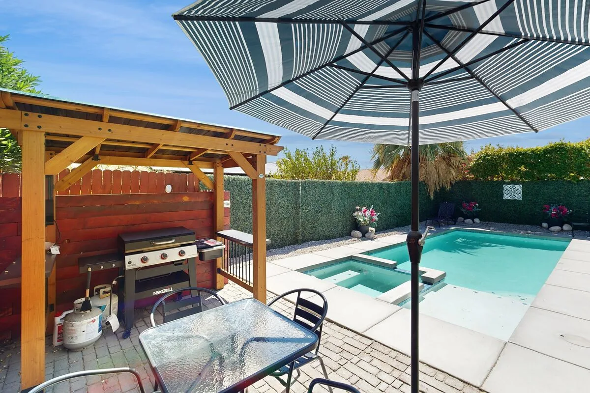 Una piscina y un patio al aire libre con zona de barbacoa sombreada y mesa de comedor.