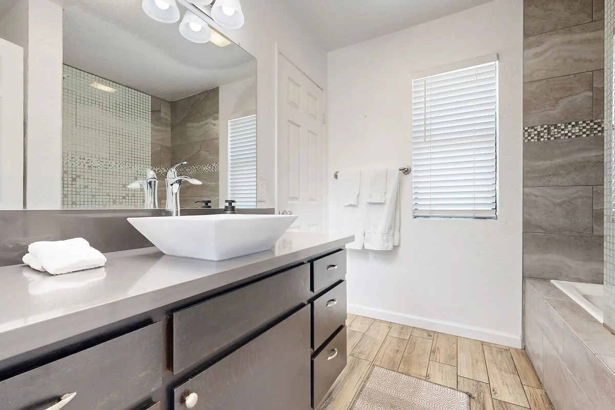 Un baño luminoso con un tocador doble, lavabo de recipiente blanco y ducha revestida de azulejos.