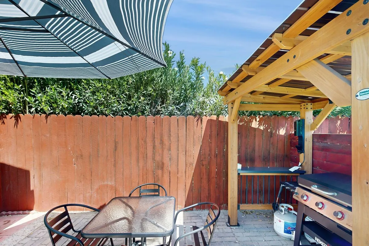Un patio al aire libre con mesa, sombrilla a rayas y parrilla.