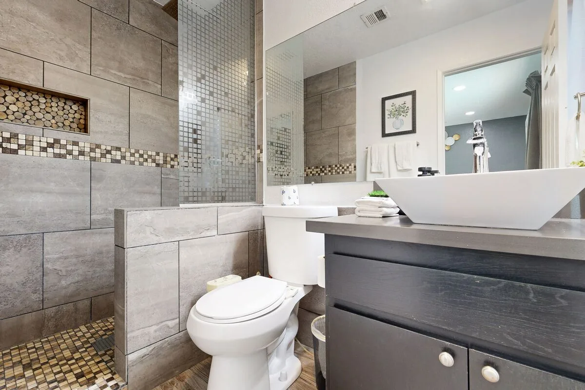 Un baño con azulejos, bañera, inodoro y tocador oscuro.
