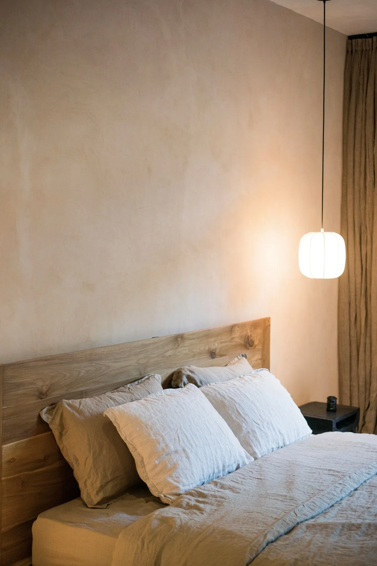 A bedroom with a wooden headboard and white bedding beneath a hanging light.