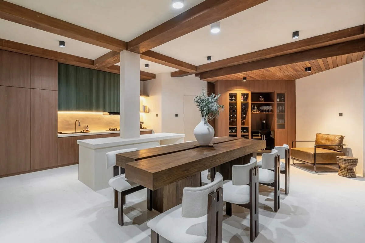 A modern open-plan kitchen and dining area with a long wooden table and bar seating.