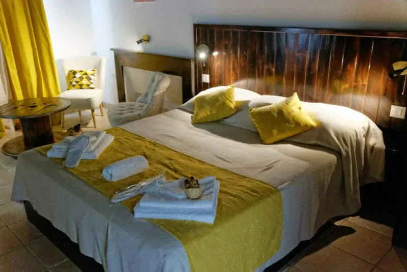 Representative hotel space: A bedroom with a double bed, yellow bedding, and a chair beside the window.
