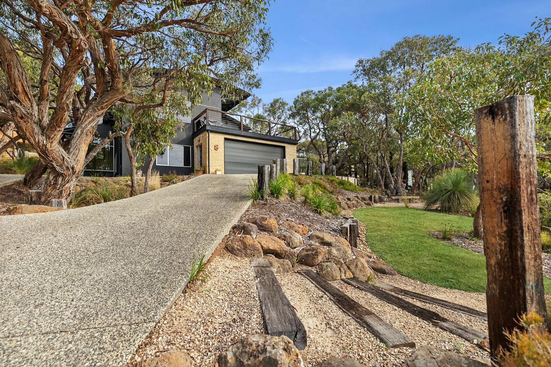 A modern house beside a landscaped lawn, with a sloped driveway in front.