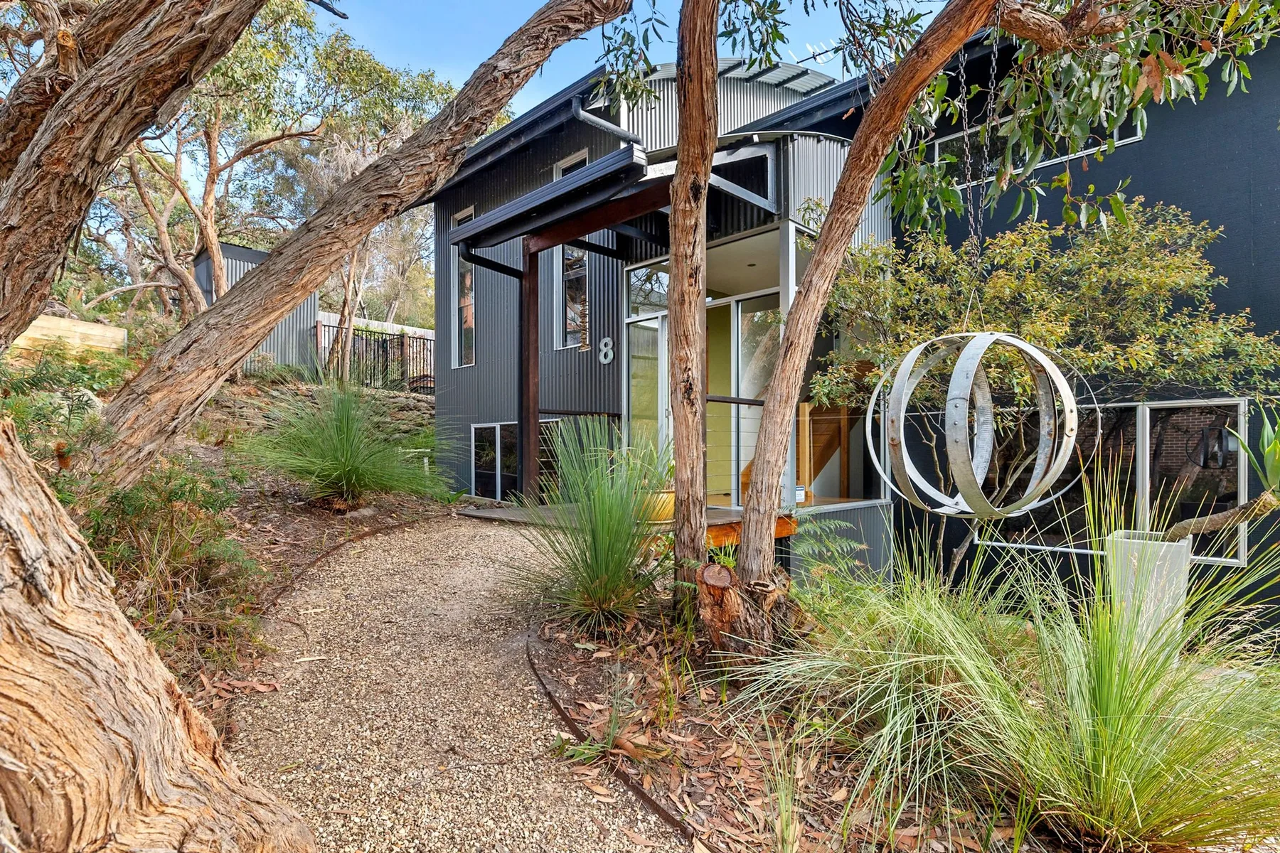 A small dark-sided building stands beside a gravel path in a landscaped garden.