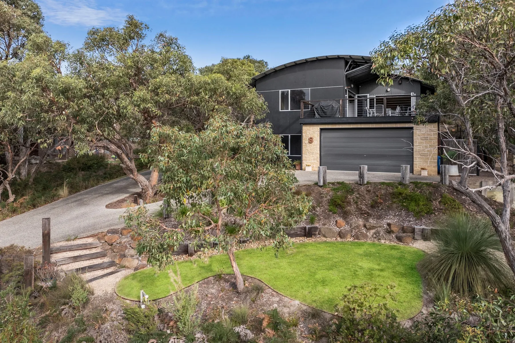 A modern house overlooks a landscaped garden with trees and a curved driveway.