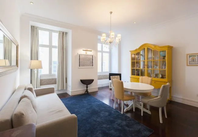 Una luminosa sala de estar y comedor con asientos alrededor de una mesa y un gabinete con puertas de vidrio.