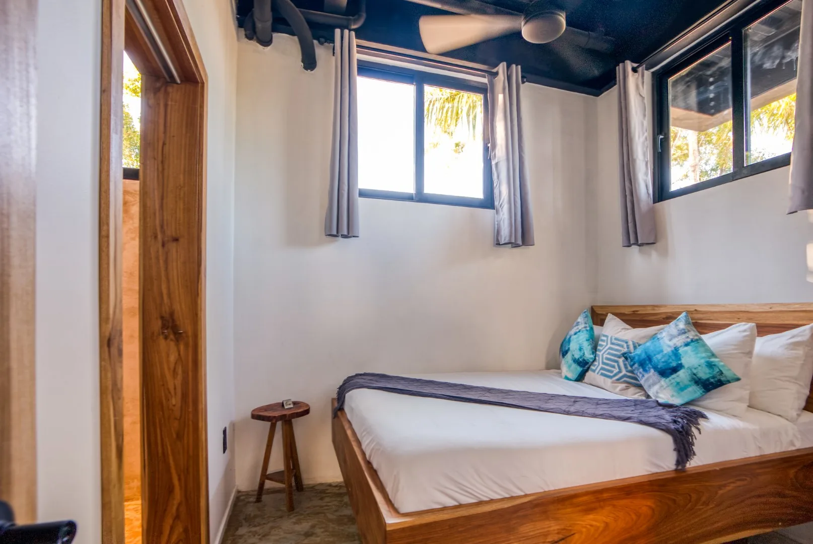 A bedroom with a wooden bed, patterned pillows, and windows with curtains.