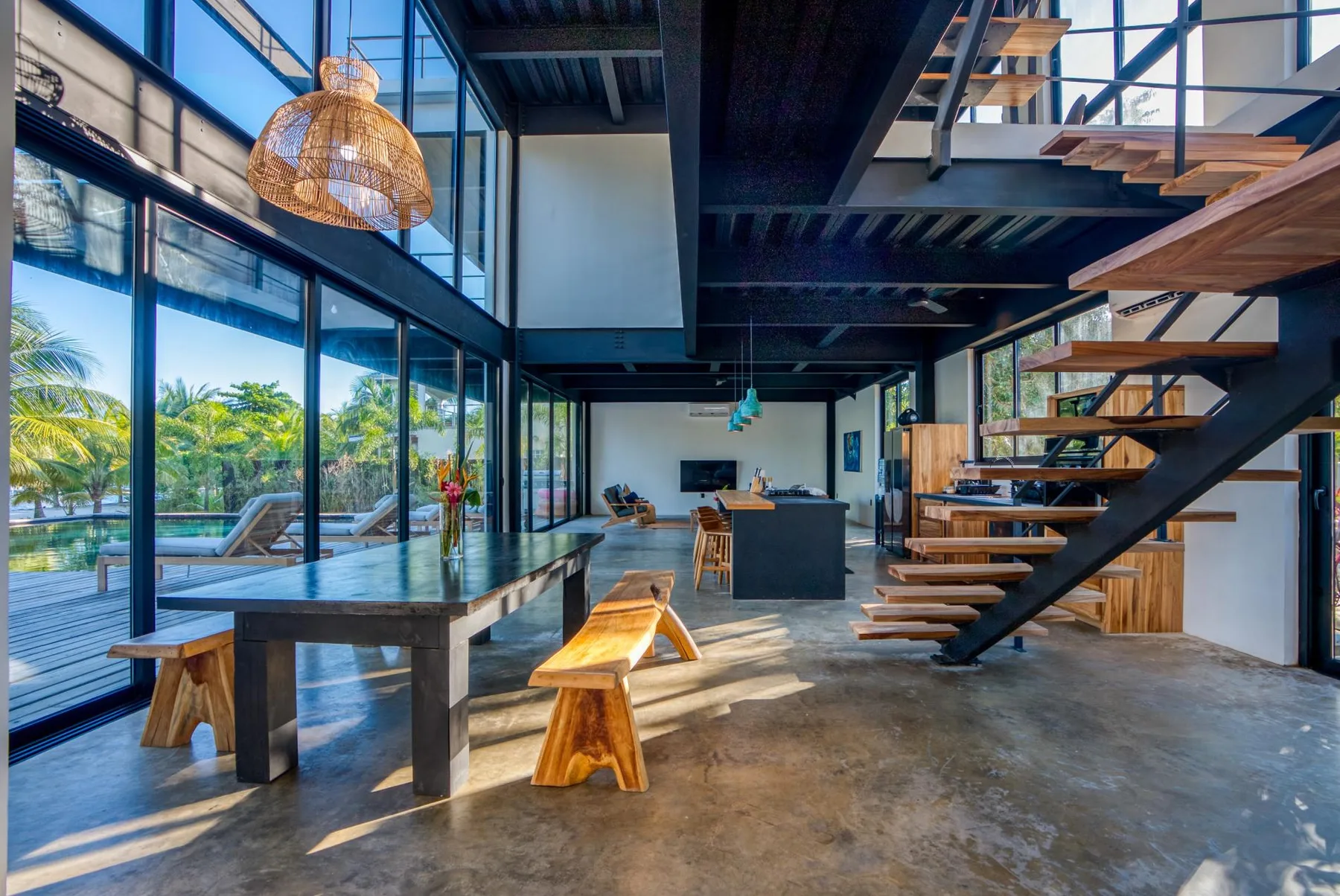 A modern open-plan interior features a dining table, kitchen island, and open staircase.