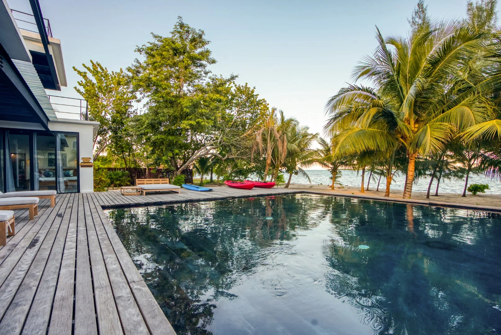 An outdoor pool beside a wooden deck, with palm trees and the sea beyond.
