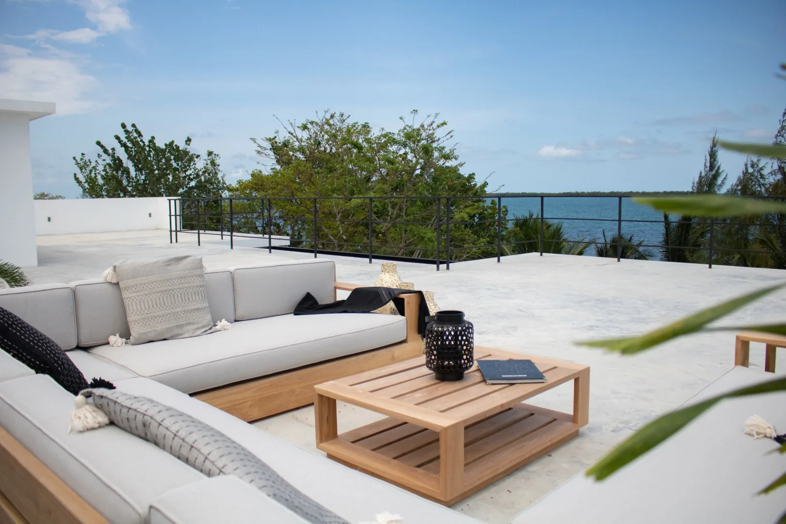 An outdoor terrace has cushioned seating and a wooden coffee table overlooking the water.