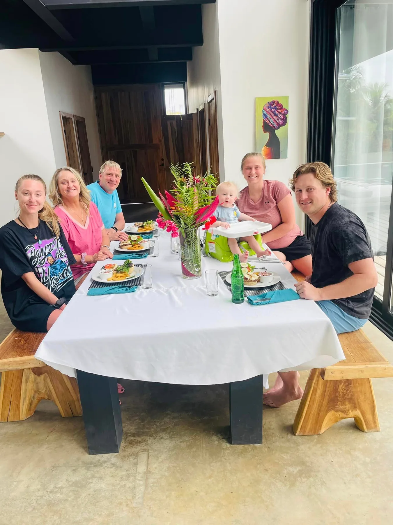 A group gathers around a dining table set with food and flowers.