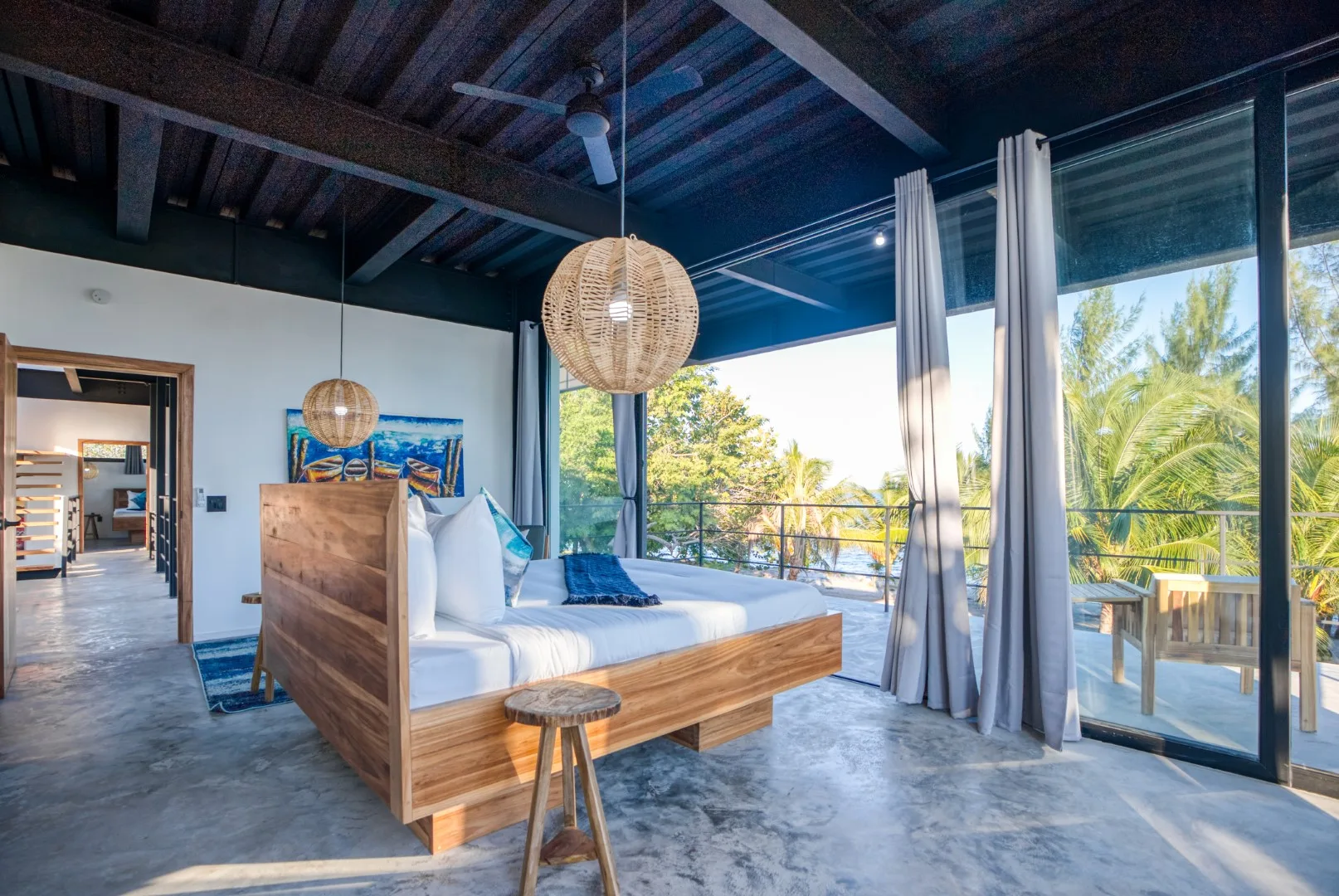 A bedroom with a wooden bed beside floor-to-ceiling windows overlooking greenery.