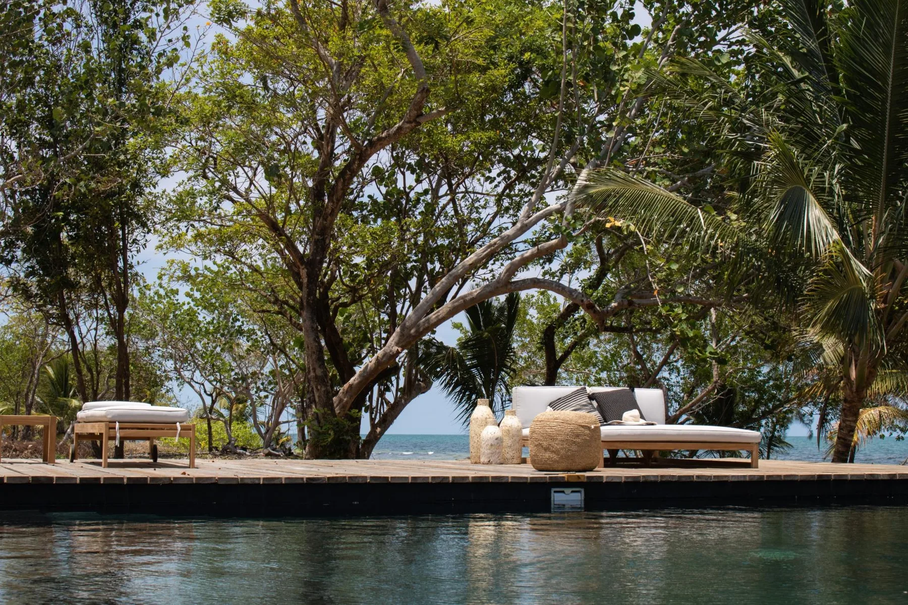 An outdoor pool beside a wooden deck with loungers and trees overlooking the sea.