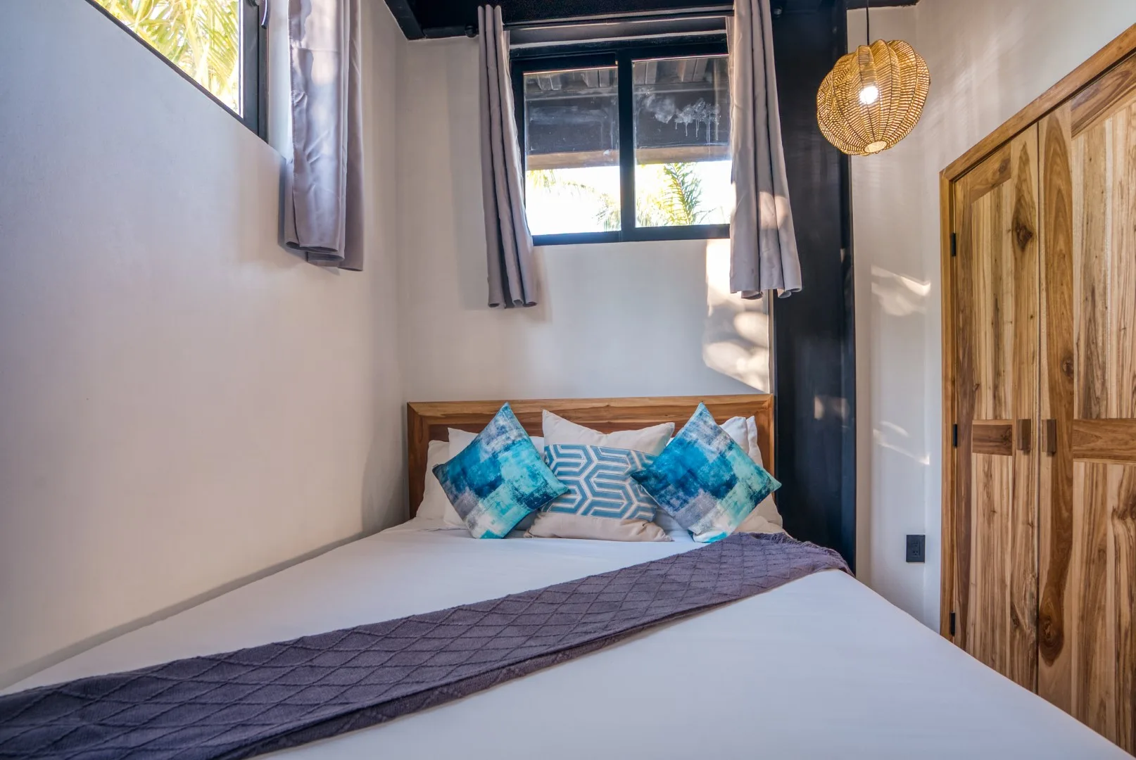 A bedroom with a bed beneath a window and wooden wardrobe.