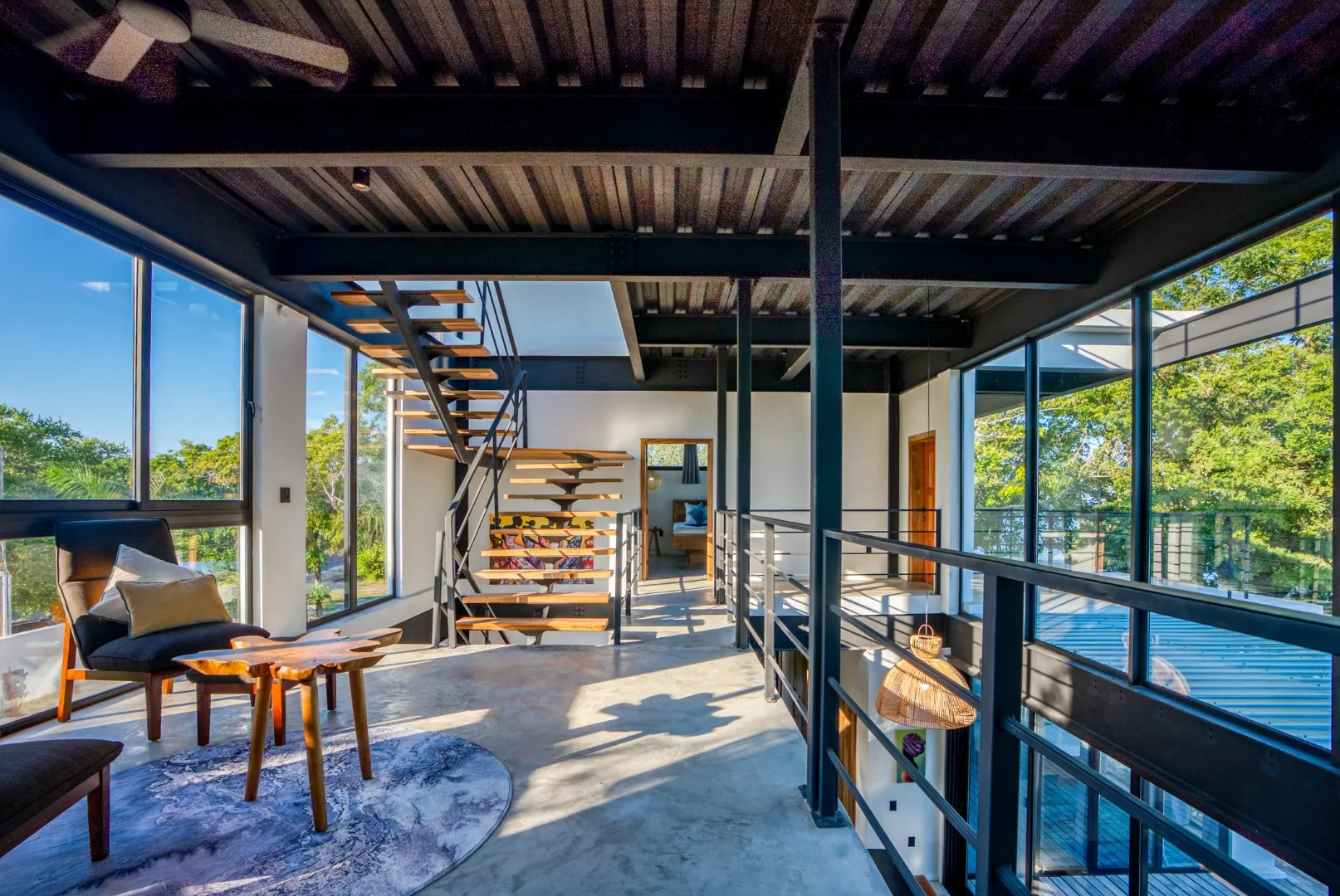 A bright glass-walled living area has an open staircase and a seating nook.