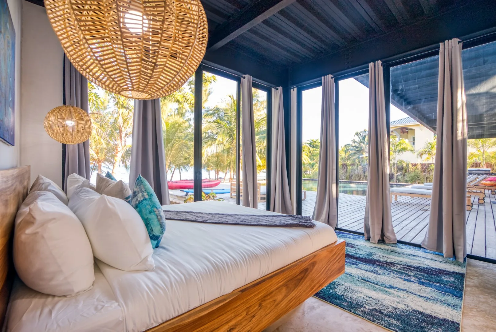 A bedroom with a bed beside large windows overlooking a pool and palm trees.