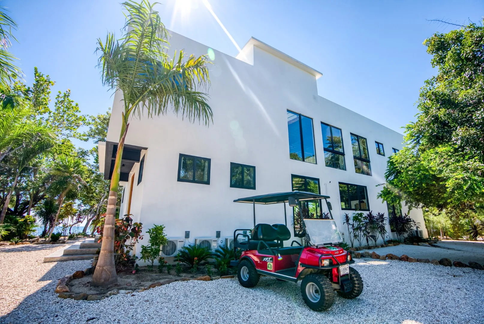 A modern white building stands among trees beside a small red utility vehicle.