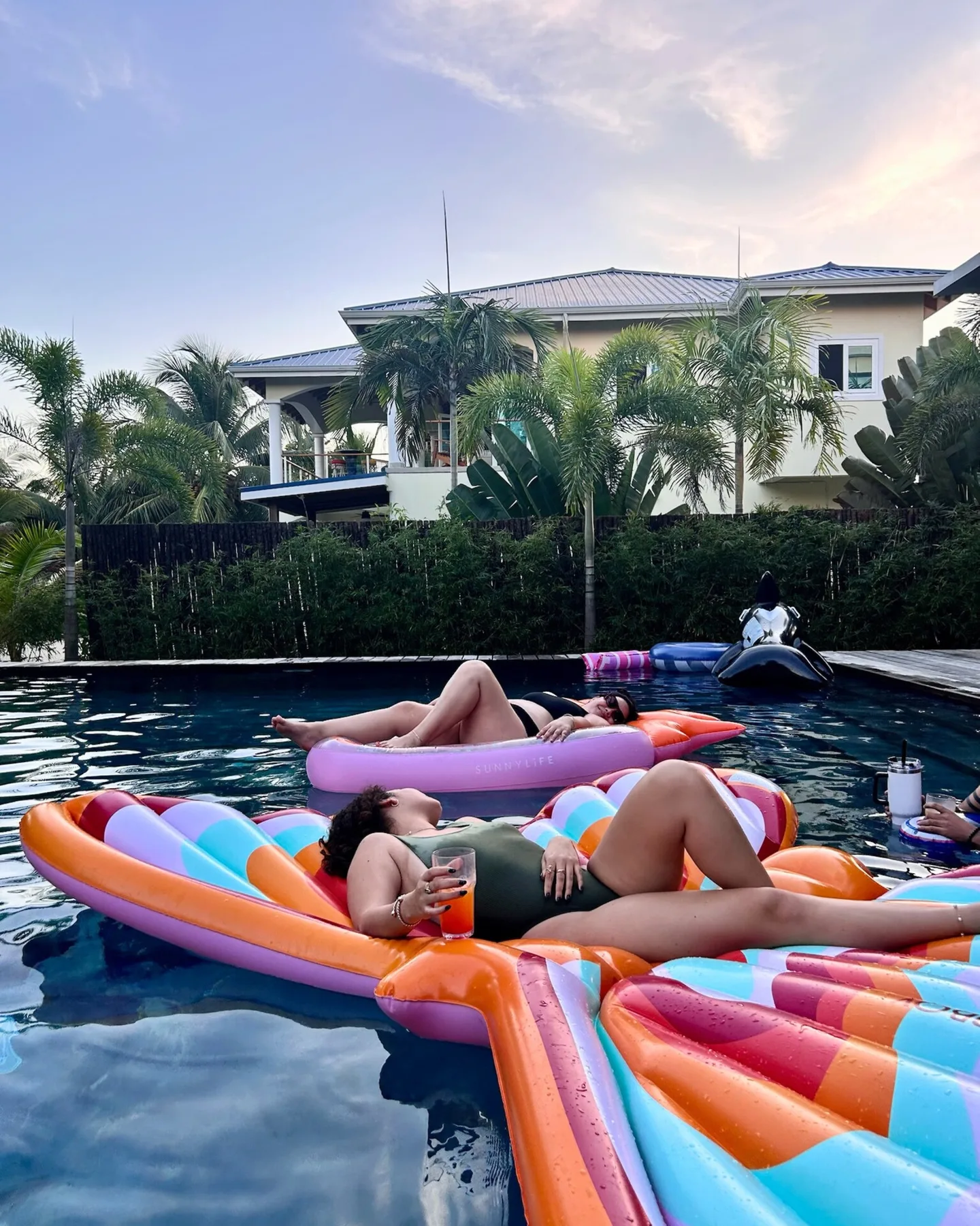 People relax on colorful inflatables in an outdoor swimming pool beside a house.