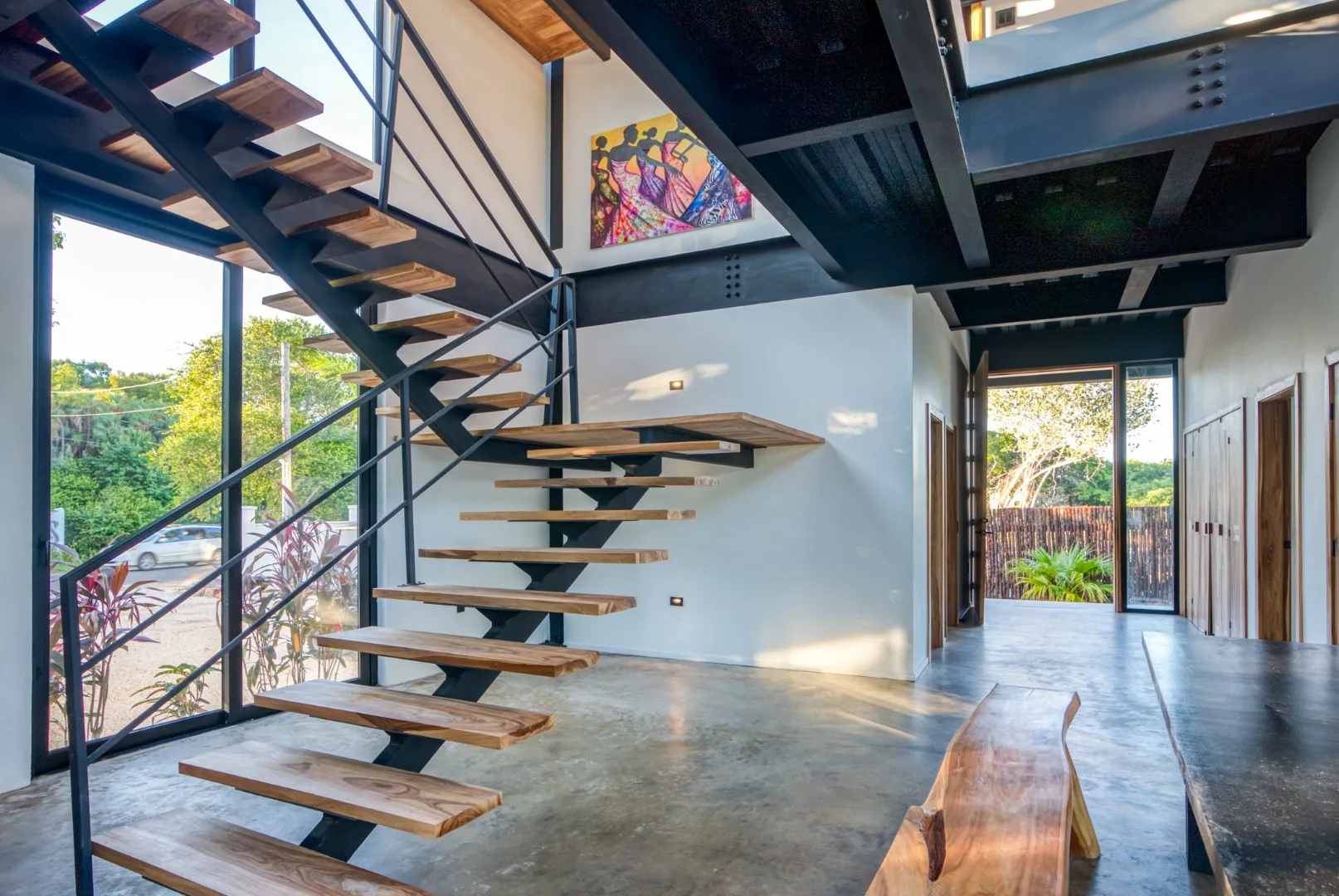 An open interior with a floating staircase, exposed beams, and a glass doorway.