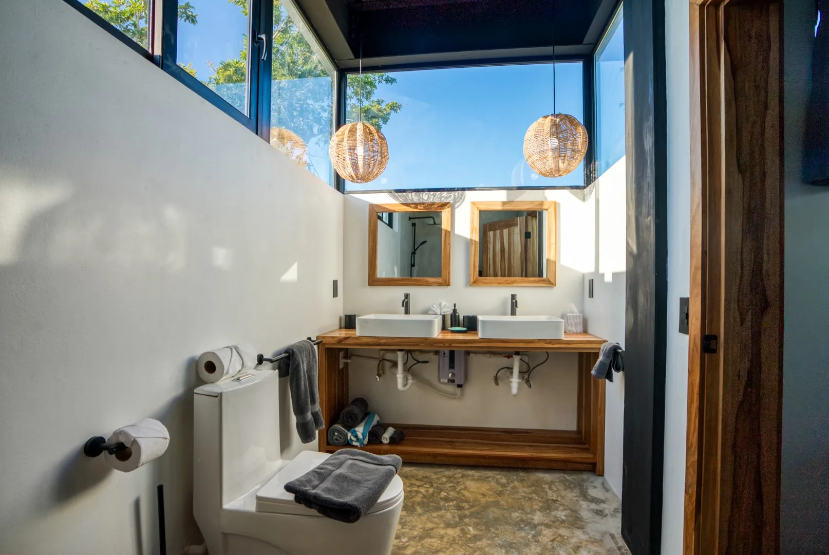 A bright bathroom with two sinks beneath tall windows and pendant lights.