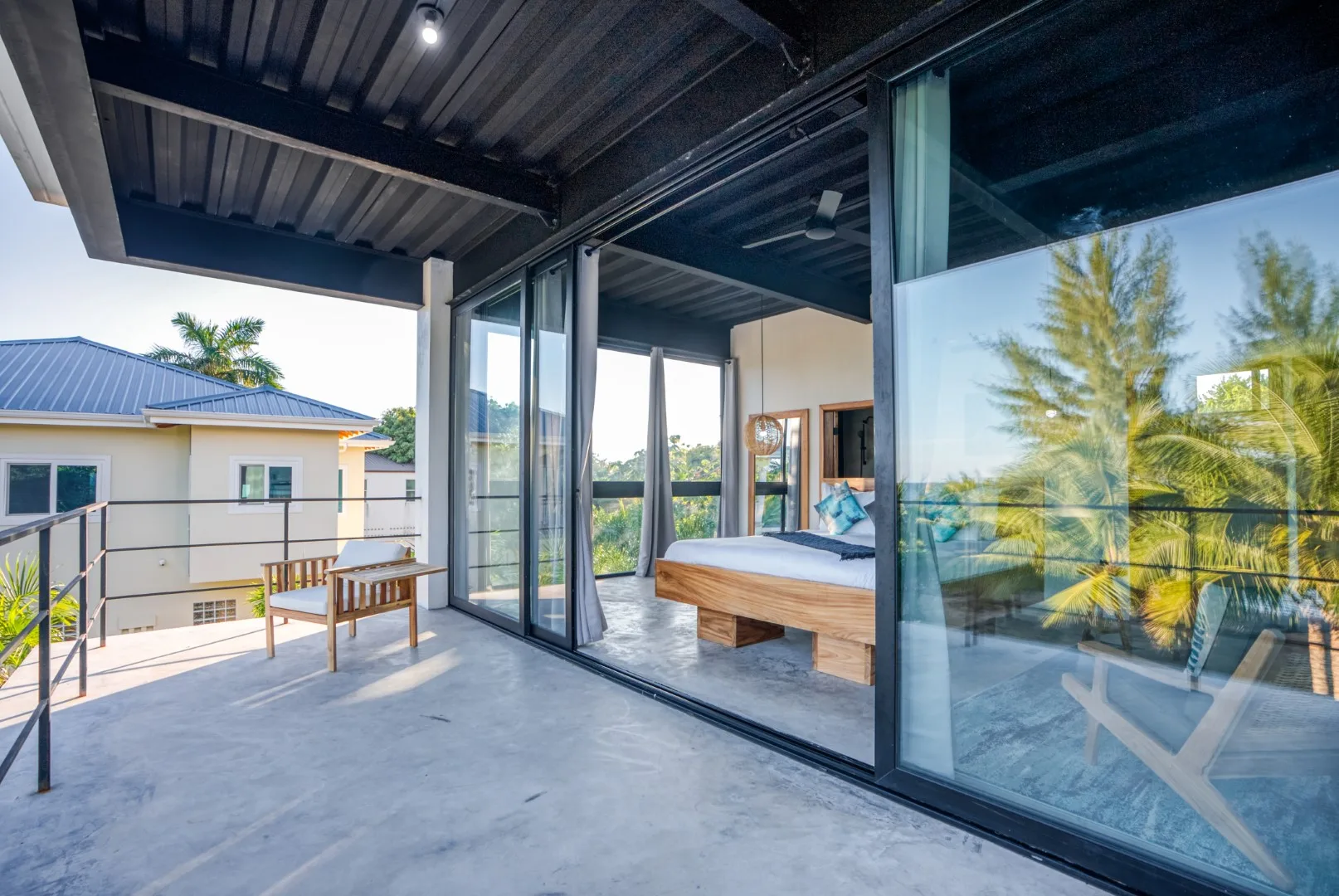 A covered patio beside a glass-walled bedroom, with a bed visible inside.