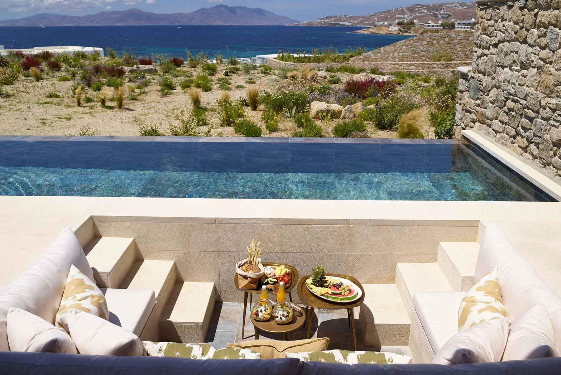 Una terraza junto al mar con piscina y una zona de asientos hundida alrededor de una mesa pequeña.