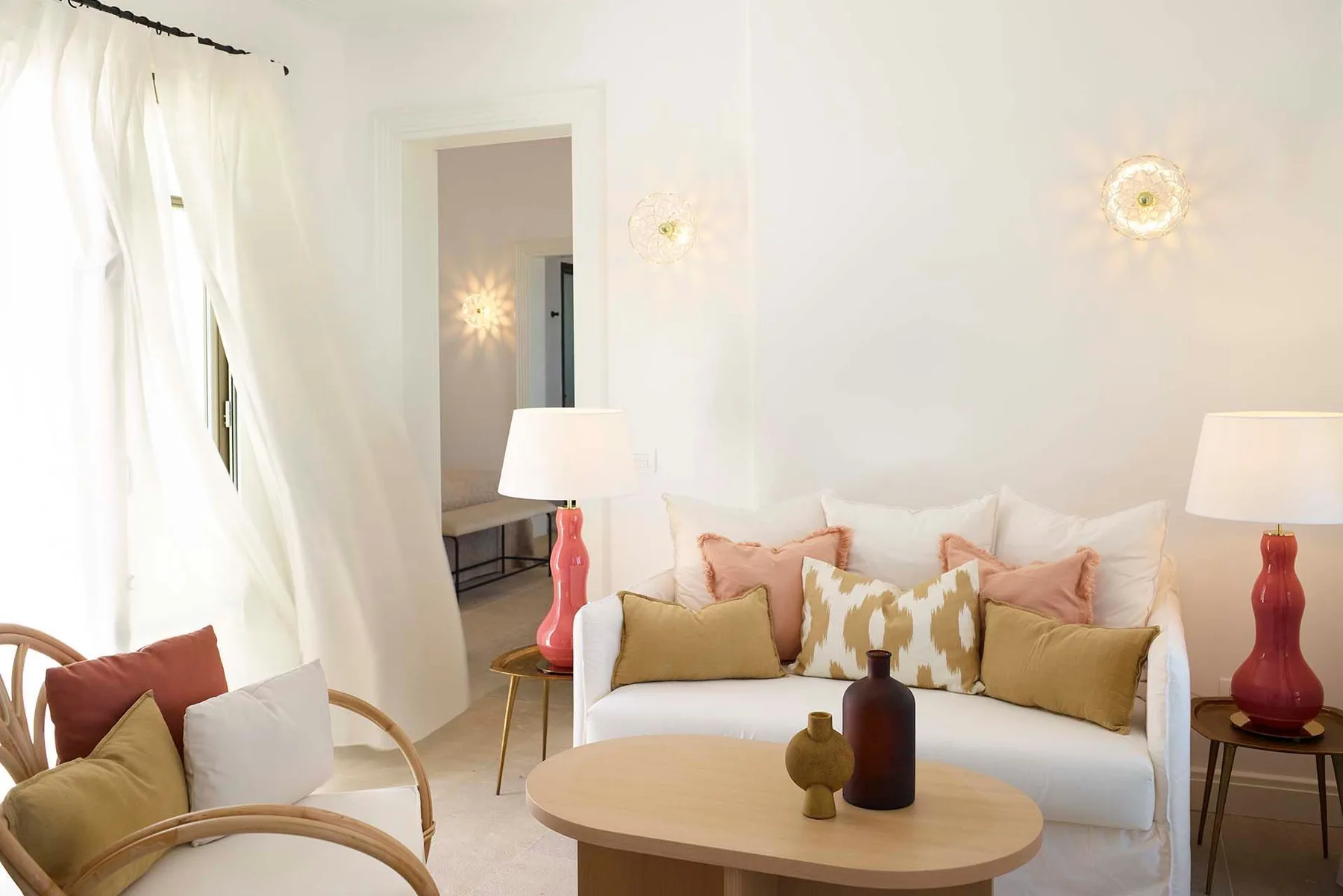Una sala de estar luminosa con un sofá blanco, cojines y una mesa de centro redonda.